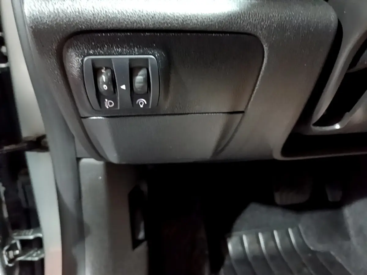 Gros plan sur les commandes de réglage des phares et du tableau de bord côté gauche d’une Renault Mégane Business Blue dCi 115 EDC gris clair.