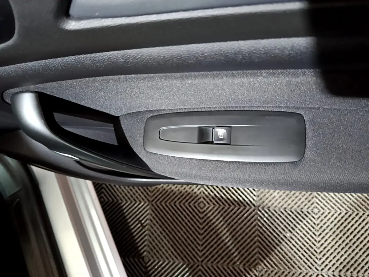 Gros plan sur la commande de lève-vitre électrique côté conducteur de la porte intérieure noire d’une Renault Mégane gris clair.