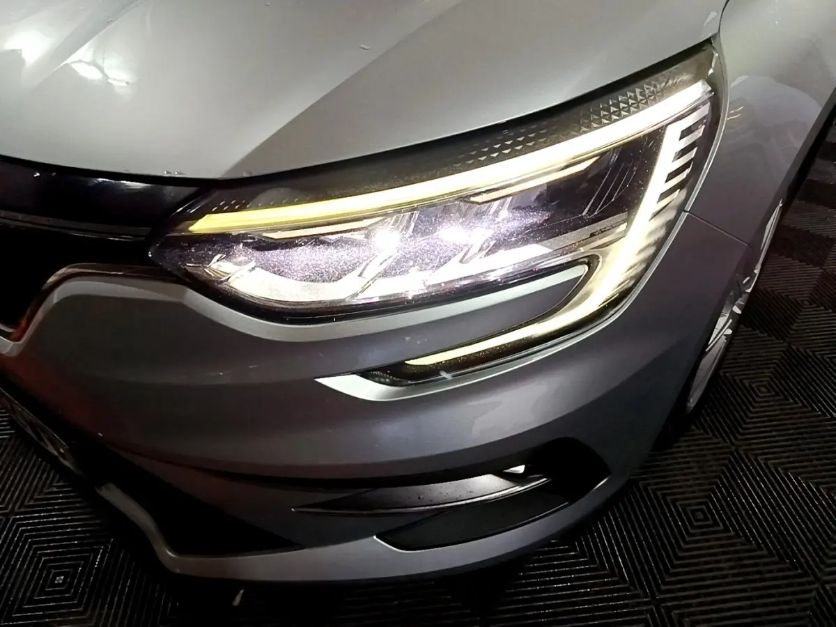 Gros plan sur le phare avant droit allumé de la Renault Mégane Business Blue dCi 115 EDC gris clair, vue en légère plongée.