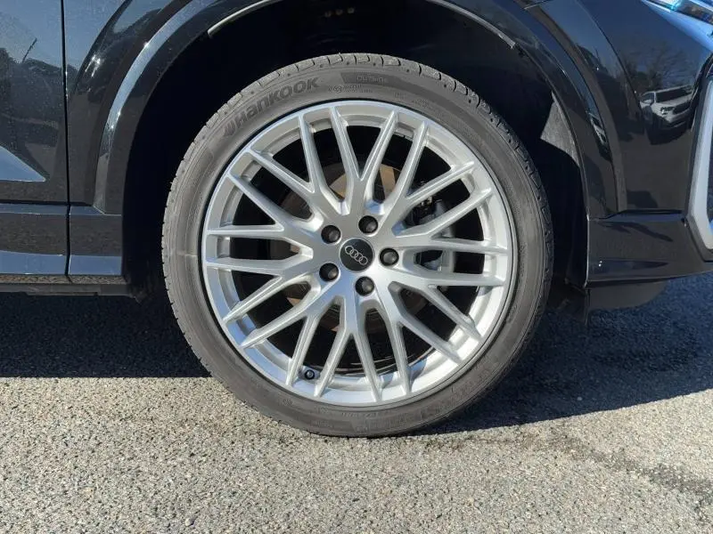 Gros plan sur la roue avant droite d’un Audi Q2 noir Mythic métallisé avec jante alu multibranches argentée.