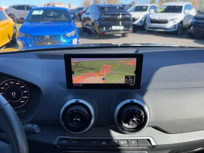 Vue intérieure du tableau de bord de l'Audi Q2 2024 avec écran GPS central et aérateurs ronds noirs.