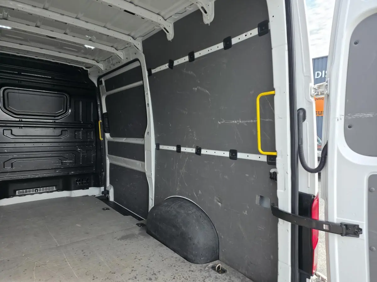 Vue intérieure arrière droite du Volkswagen Crafter blanc, montrant l'espace de chargement avec plancher bois et protections latérales noires.