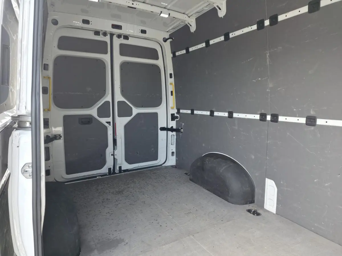 Vue intérieure arrière du fourgon Volkswagen Crafter blanc, montrant l'espace de chargement avec plancher et parois protégés.