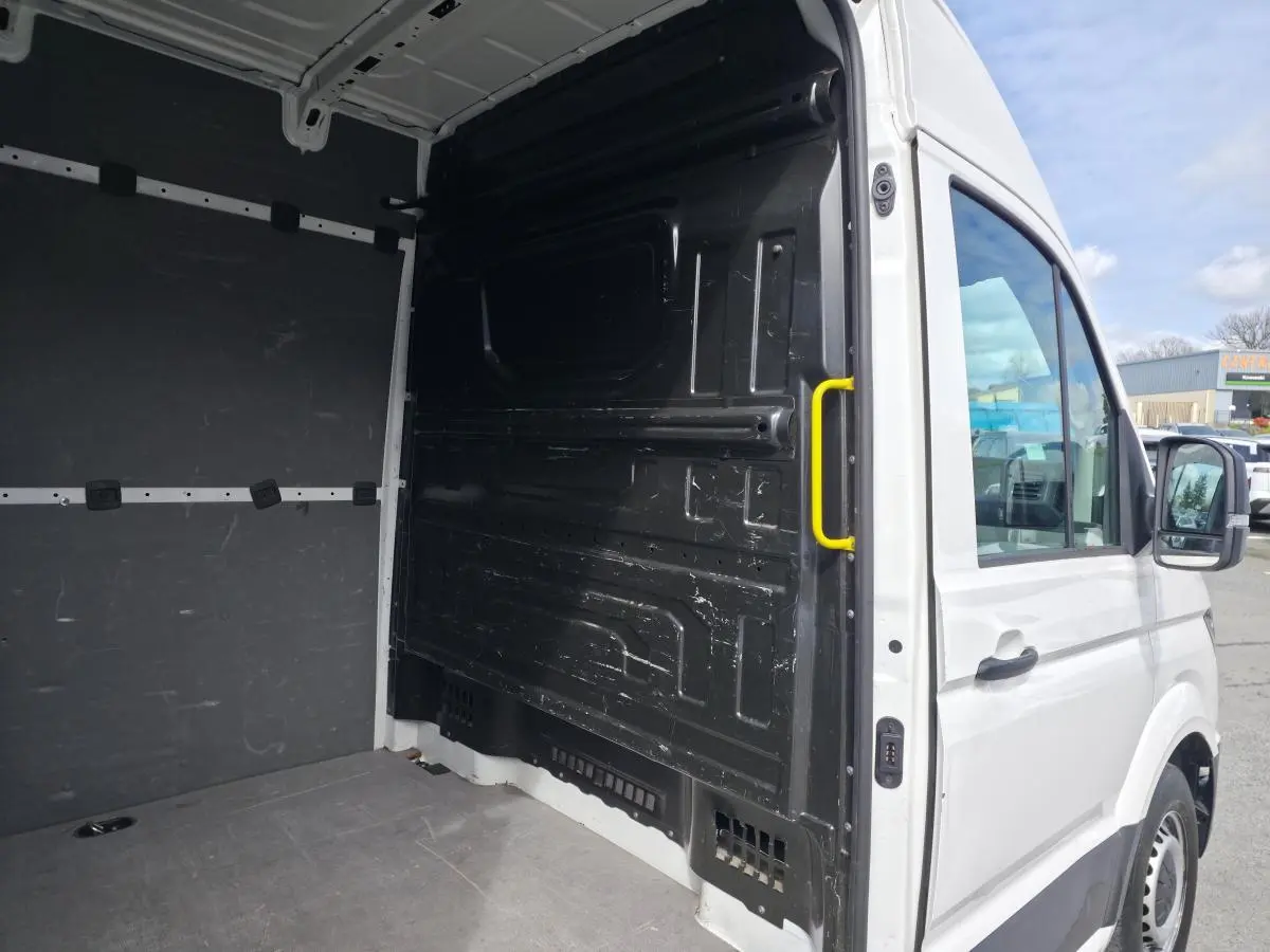 Vue intérieure arrière droite du Volkswagen Crafter blanc avec plancher bois et poignée jaune sur cloison de séparation.
