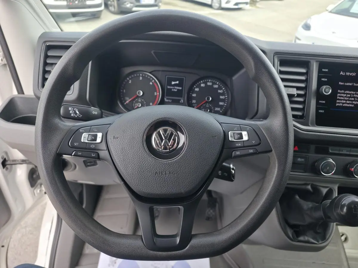 Vue intérieure centrée sur le volant noir Volkswagen et le tableau de bord du fourgon blanc Volkswagen Crafter 2023.