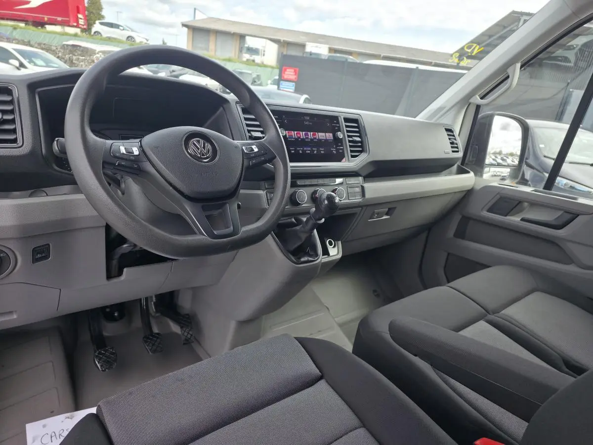 Vue intérieure côté conducteur du Volkswagen Crafter Fourgon blanc 2023, tableau de bord et volant multifonctions visibles.
