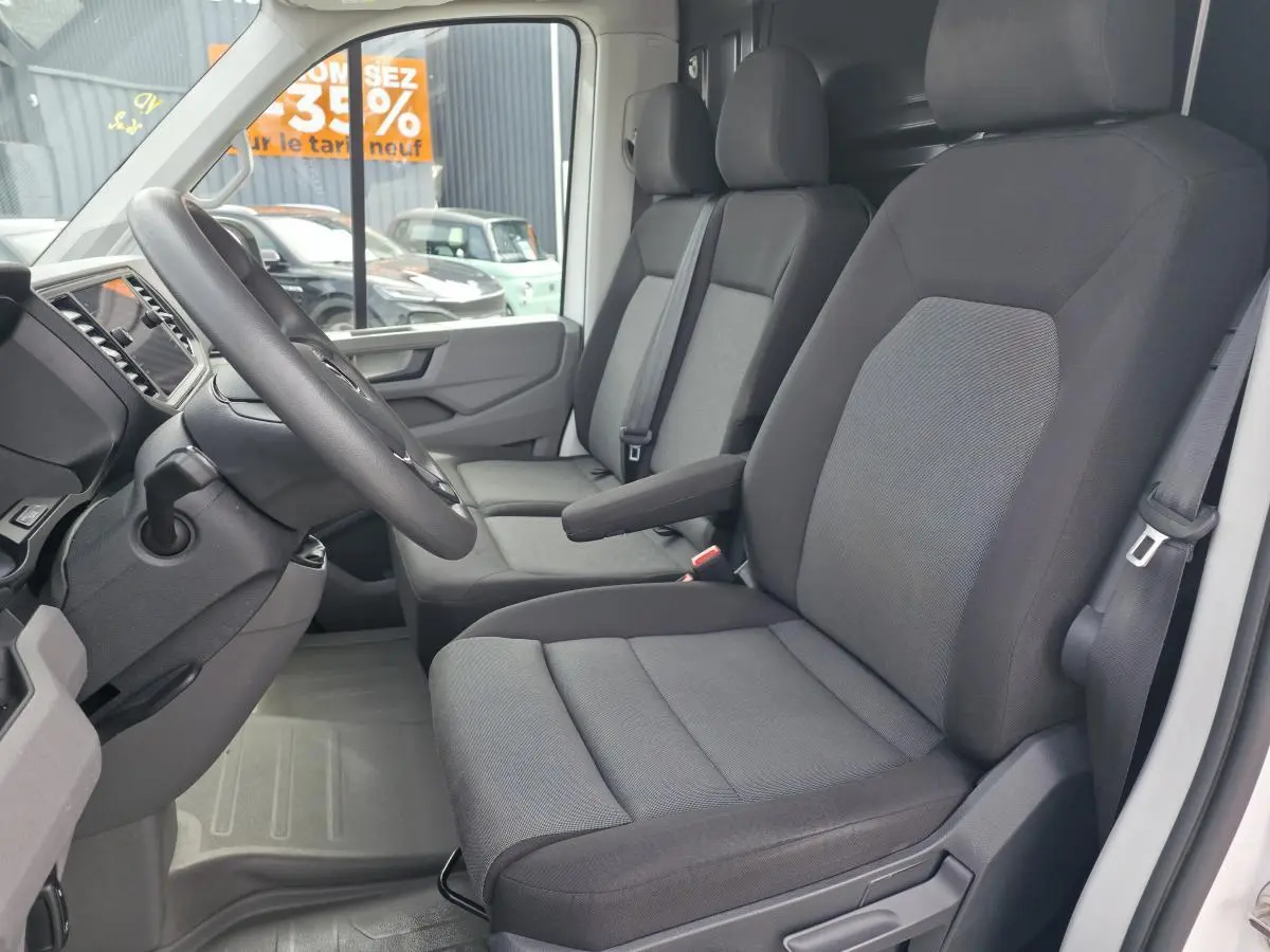 Vue intérieure côté conducteur du Volkswagen Crafter Fourgon blanc 2023, montrant les sièges tissu gris et le volant multifonctions.