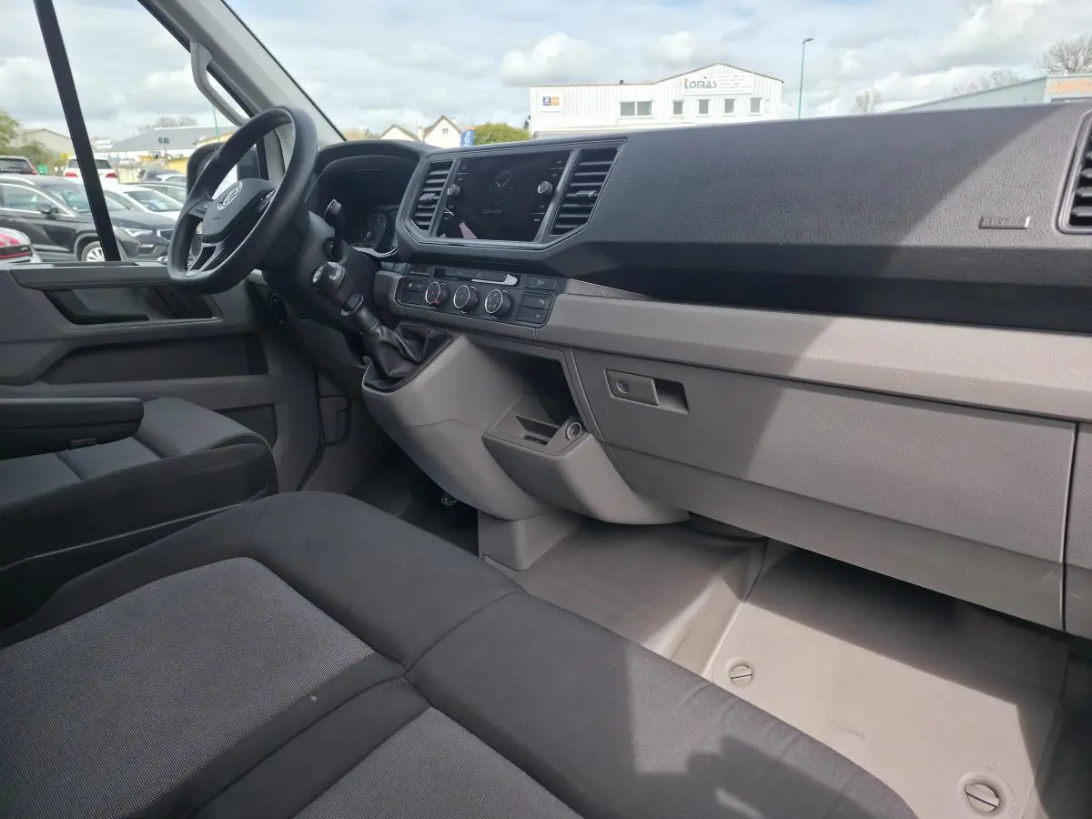 Vue intérieure côté conducteur du Volkswagen Crafter Fourgon 2023 avec tableau de bord gris et sièges tissu noirs.