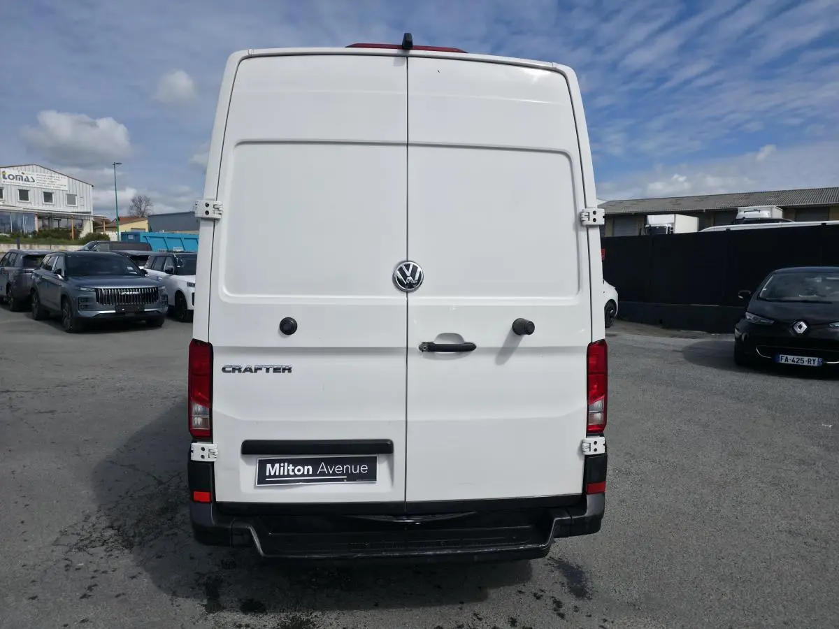 Vue arrière d’un Volkswagen Crafter fourgon blanc avec portes battantes et logo centré sous ciel partiellement nuageux.