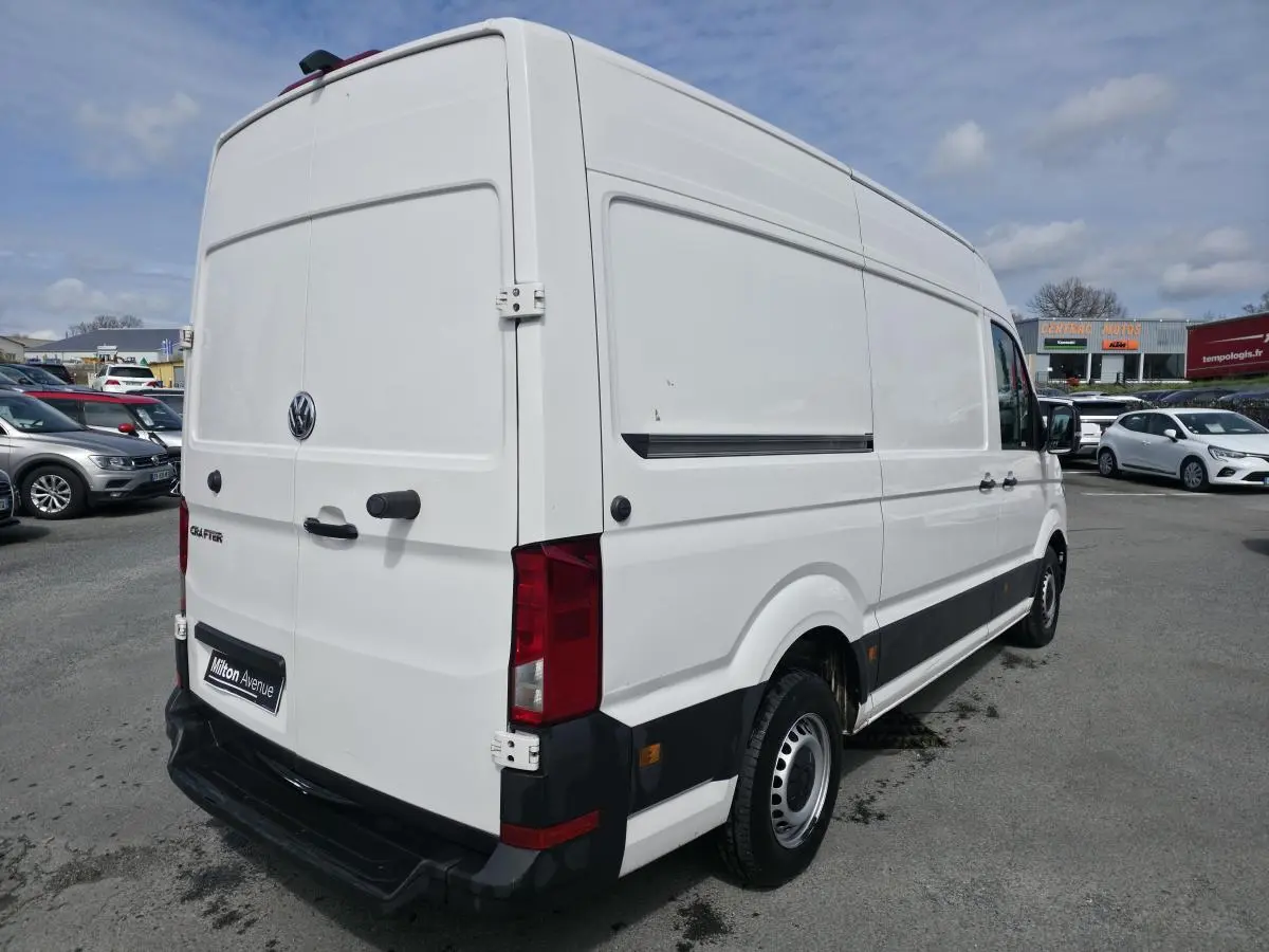 Vue 3/4 arrière droite d'un Volkswagen Crafter blanc avec portes battantes arrière et protections latérales noires.