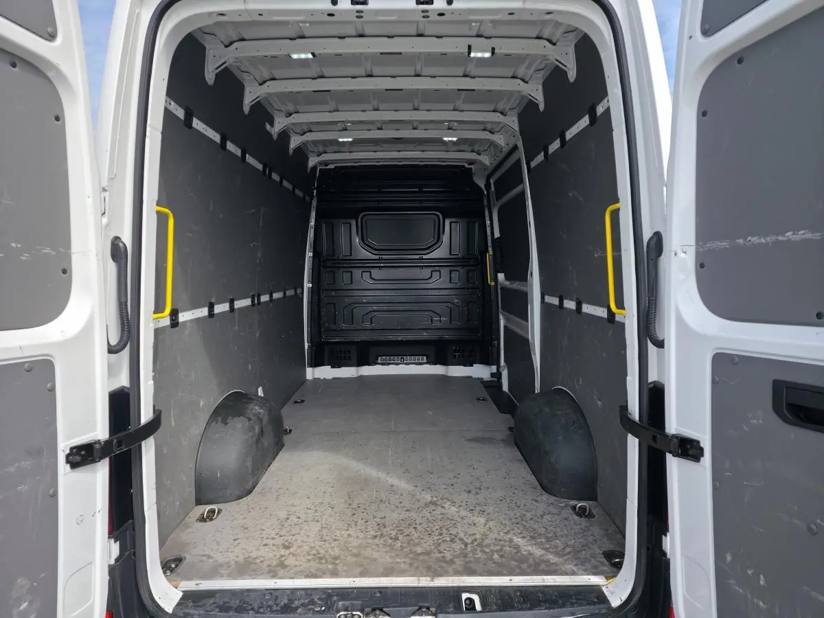 Vue intérieure arrière du Volkswagen Crafter blanc, montrant l'espace de chargement avec plancher bois et protections latérales grises.