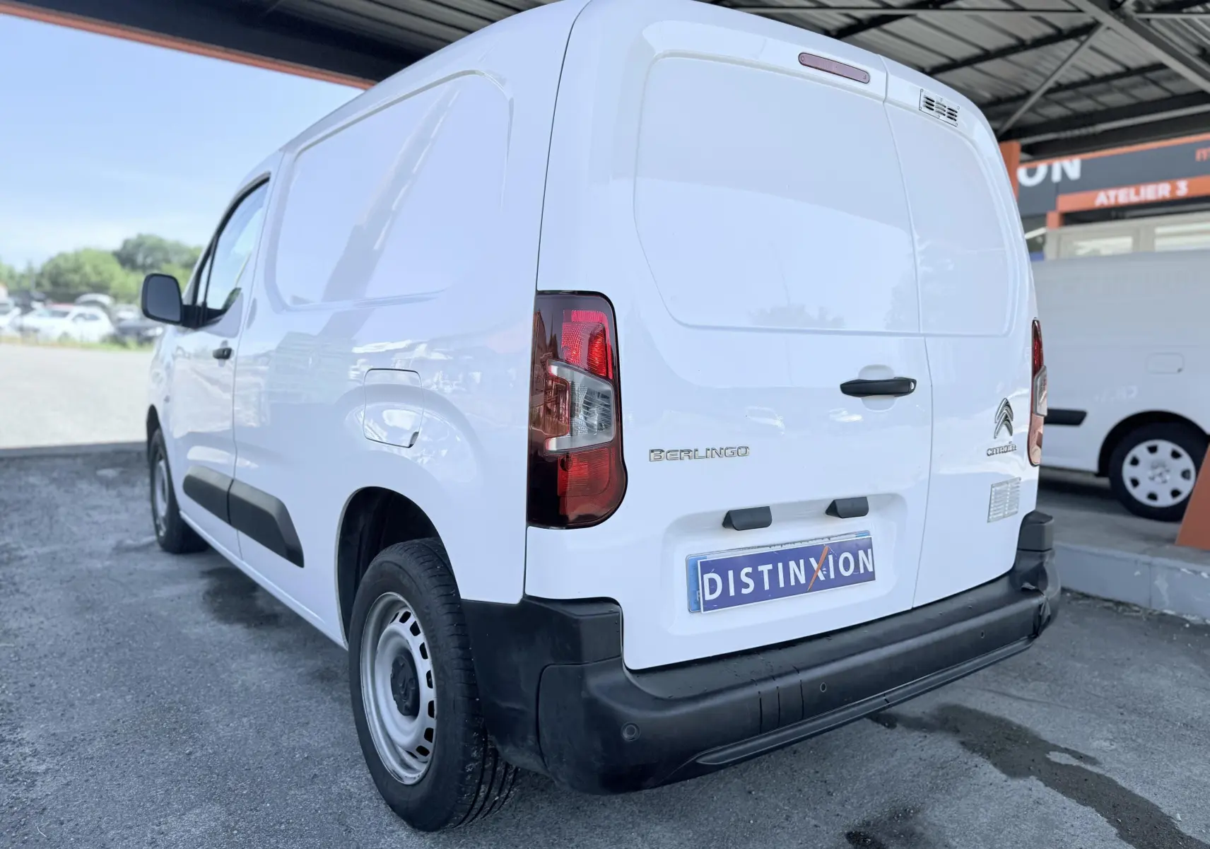 Vue 3/4 arrière droite d’un utilitaire Citroën Berlingo blanc avec pare-chocs noir et plaque Distinxion.