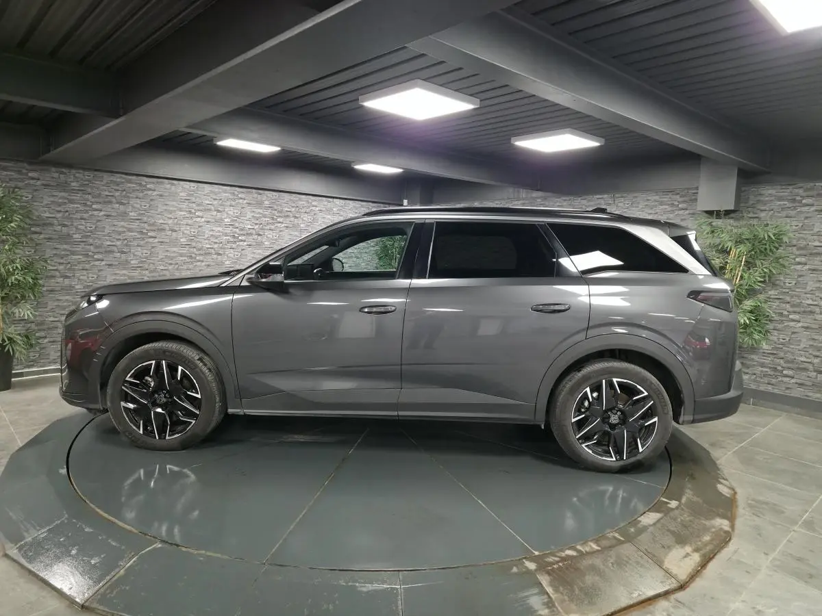 Vue latérale droite d'un Peugeot 5008 gris métallisé avec jantes alliage noires et barres de toit noires brillantes.