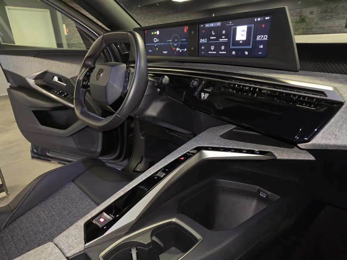 Vue intérieure côté conducteur du Peugeot 5008 2025 hybride, avec tableau de bord numérique panoramique et sellerie tissu gris.