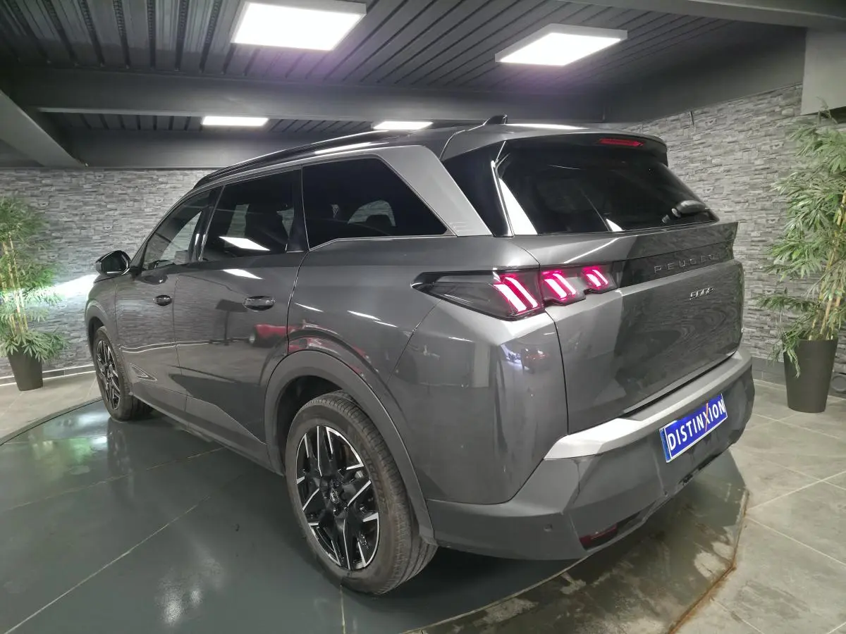 Vue 3/4 arrière droite d'un Peugeot 5008 gris métallisé avec feux arrière à LED en forme de griffes et jantes alliage noires.