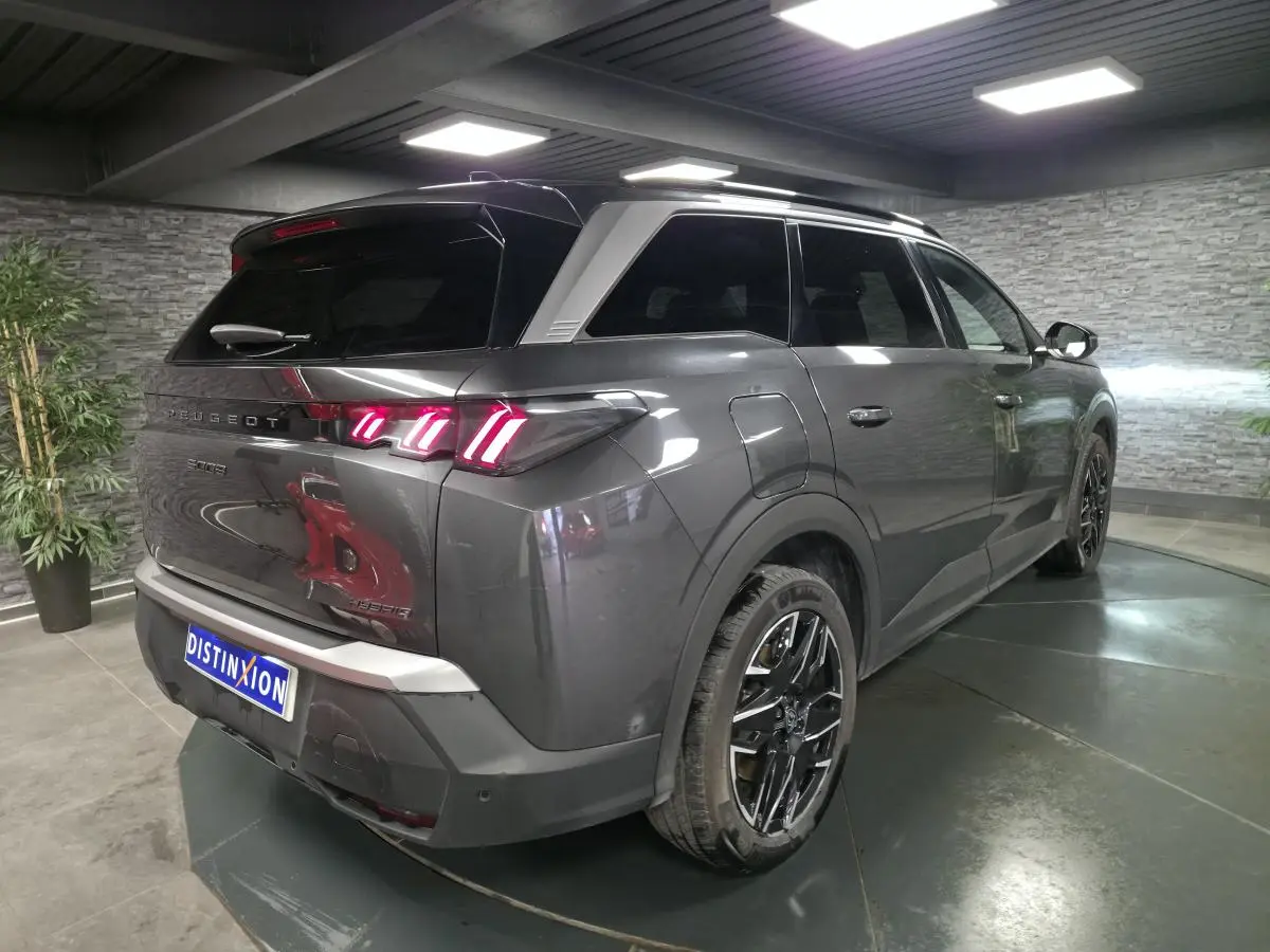 Vue 3/4 arrière droite d’un Peugeot 5008 gris métallisé avec feux arrière LED 3 griffes et jantes alliage noires.
