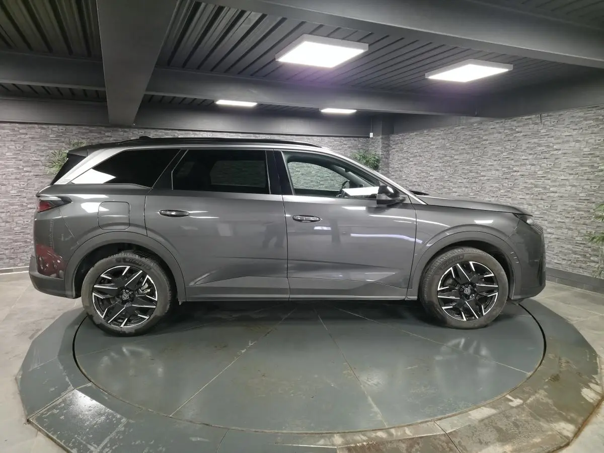 Vue de profil côté gauche d’un Peugeot 5008 gris métallisé avec jantes alliage 19 pouces et barres de toit noires.