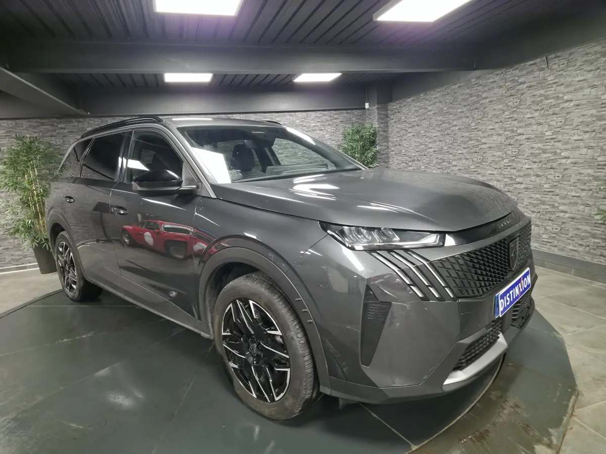 Vue 3/4 avant droite d’un Peugeot 5008 gris métallisé avec jantes alliage noires et calandre noire distinctive.