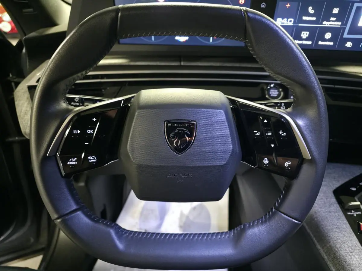 Vue rapprochée du volant noir cuir du Peugeot 5008 2025 avec commandes intégrées et logo central.