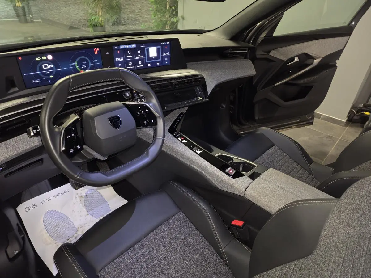 Vue intérieure côté conducteur du Peugeot 5008 2025, mettant en valeur le tableau de bord numérique et la sellerie tissu gris et cuir noir.