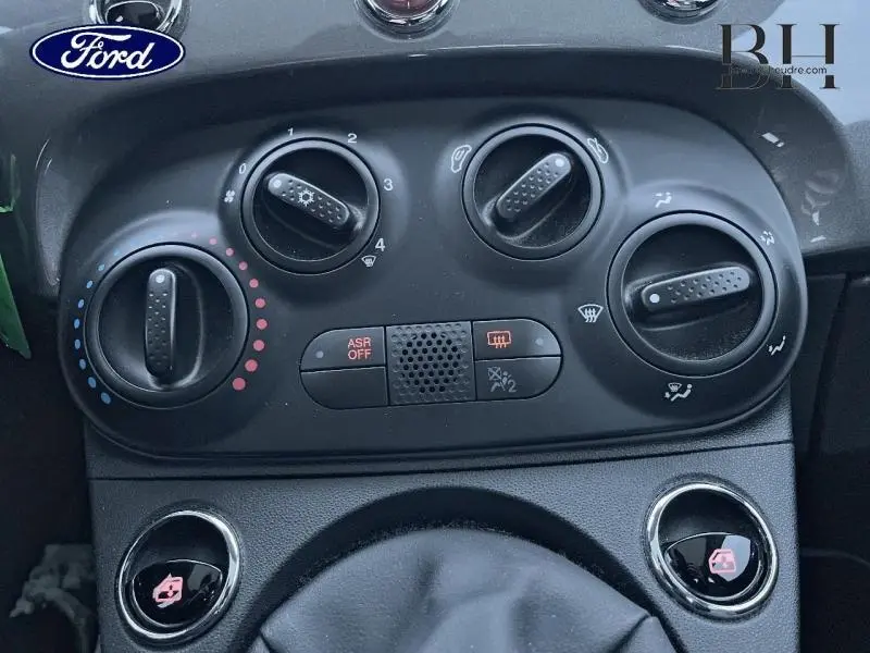 Gros plan sur les commandes de climatisation et ventilation noires du tableau de bord d’une Fiat 500 grise.