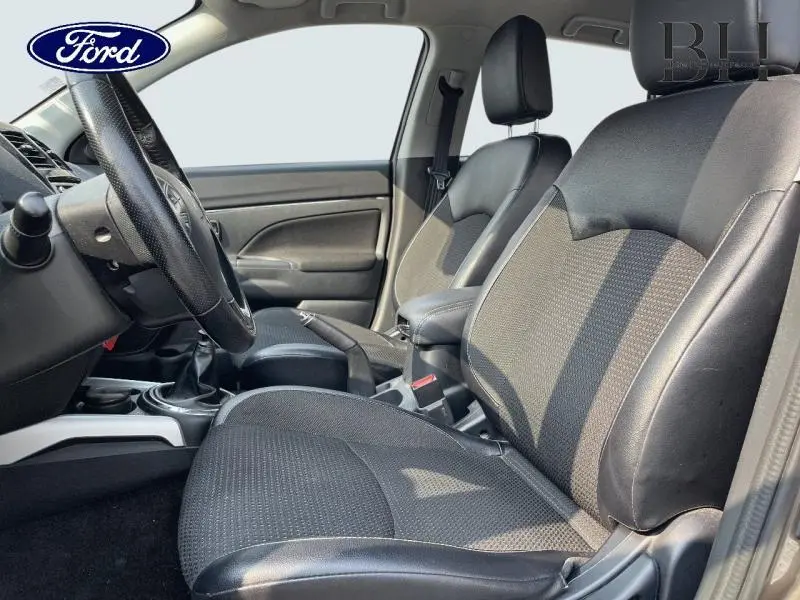 Vue intérieure côté conducteur montrant les sièges en tissu et cuir noir avec accoudoir central, volant cuir et levier de vitesse.