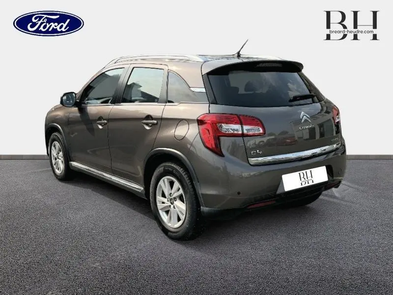 Vue 3/4 arrière droite d'un Citroën C4 Aircross brun Mangaro avec barres de toit et vitres arrière surteintées.