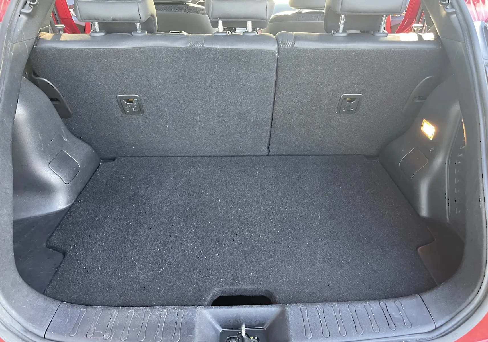 Coffre ouvert vu de l'arrière d'un Nissan Juke rouge 2017, avec intérieur noir et éclairage latéral allumé.