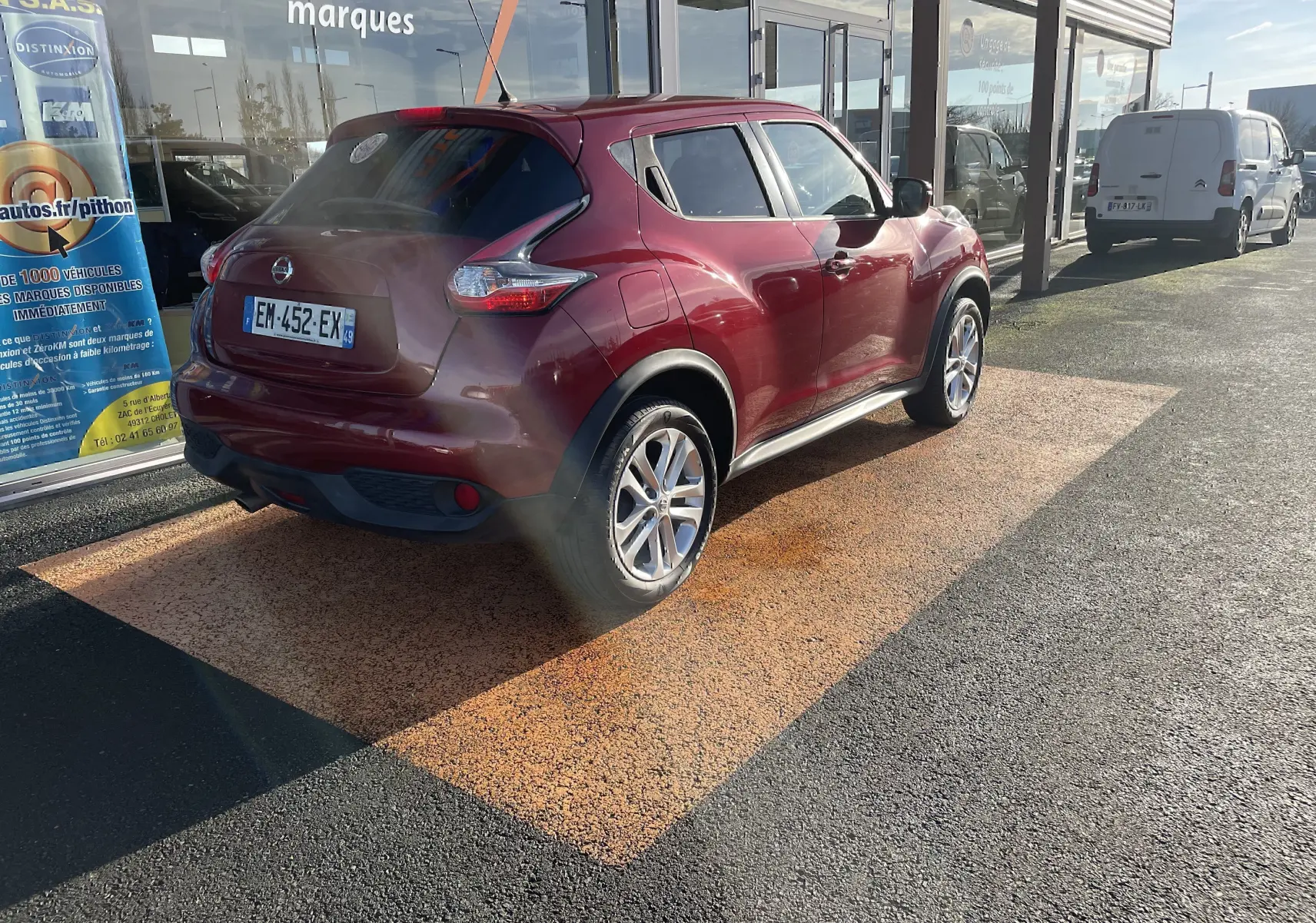 Nissan Juke rouge vue 3/4 arrière droit, stationné devant un bâtiment avec vitres réfléchissantes.