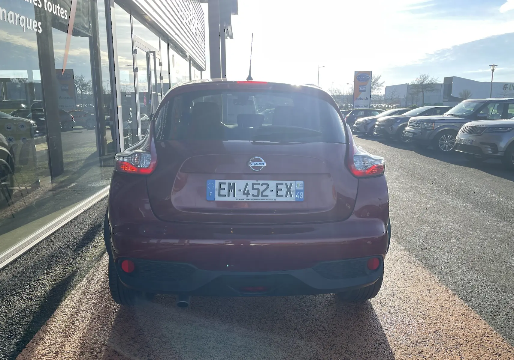 Vue arrière d'un Nissan Juke rouge 2017 garé devant une vitrine, avec feux arrière allumés et plaque visible.