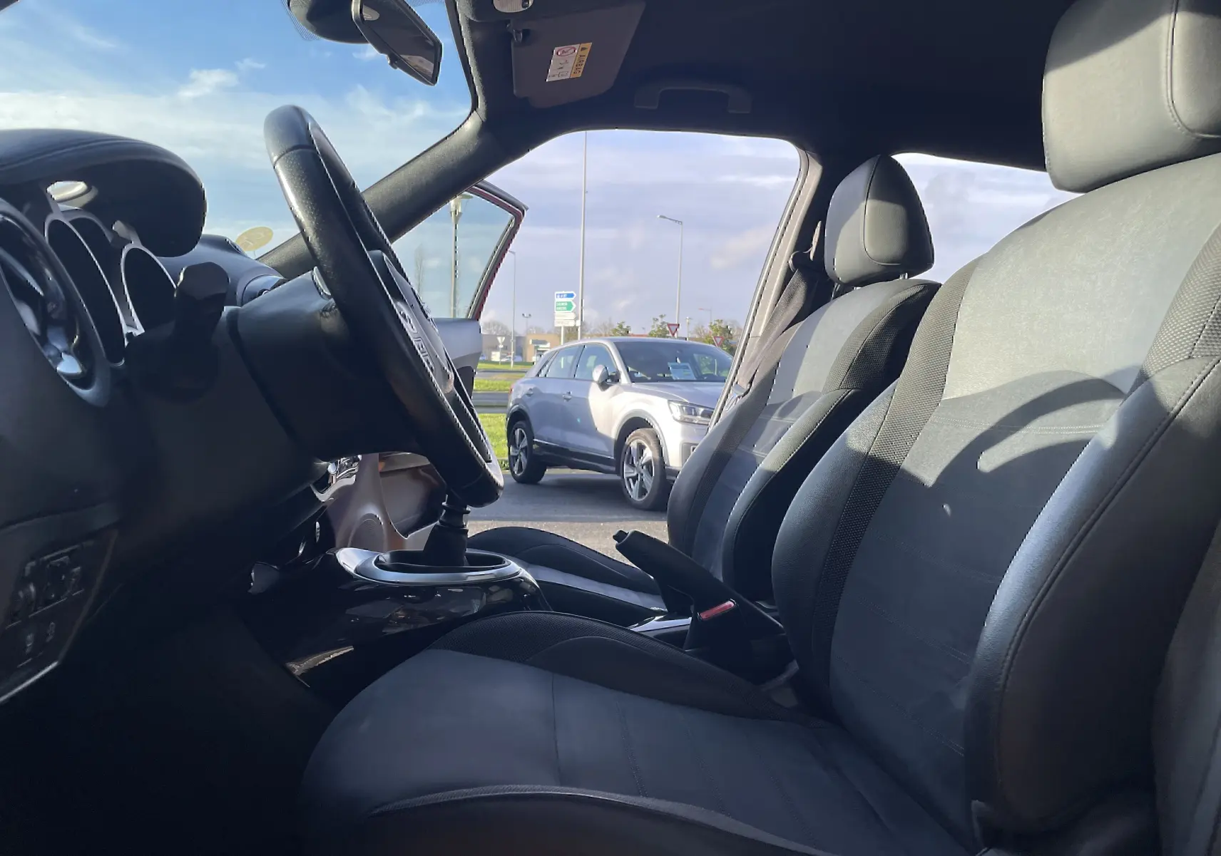 Vue intérieure côté conducteur du Nissan Juke rouge 2017, mettant en valeur les sièges gris-noir et la boîte manuelle.