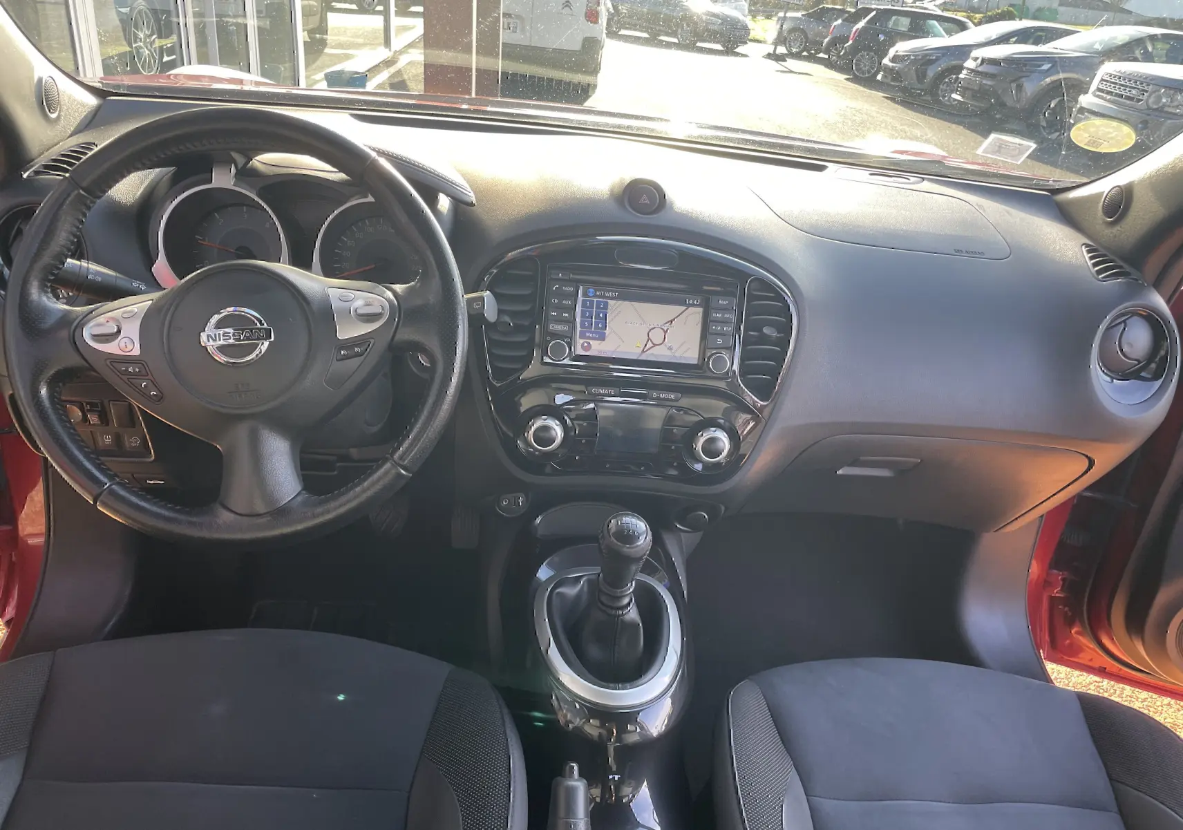 Vue intérieure avant du Nissan Juke rouge 2017, mettant en valeur le volant, la console centrale avec GPS et la boîte manuelle.