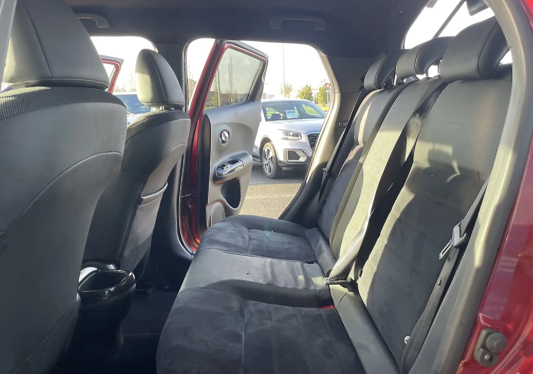 Vue intérieure côté droit montrant la banquette arrière noire du Nissan Juke rouge avec porte arrière ouverte.