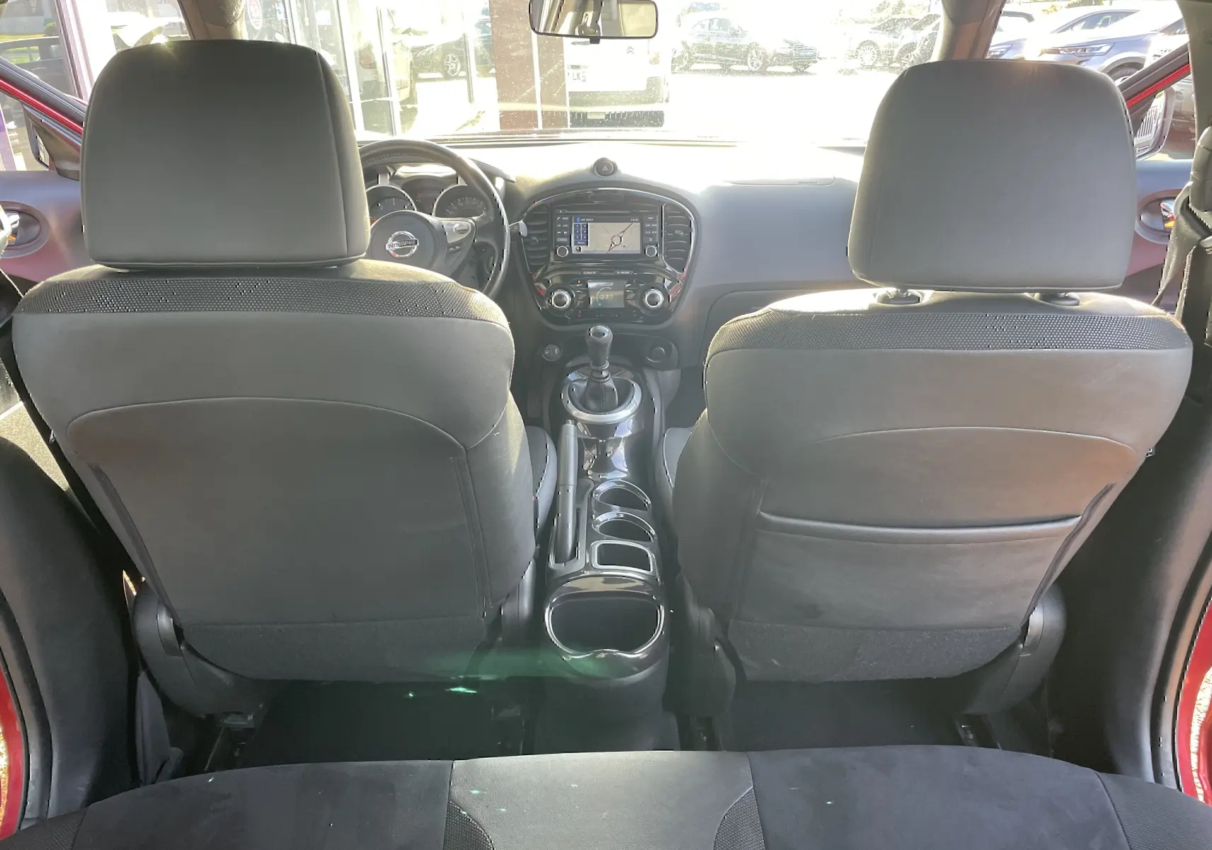 Vue intérieure arrière du Nissan Juke rouge 2017, mettant en valeur la console centrale avec boîte manuelle et écran GPS.