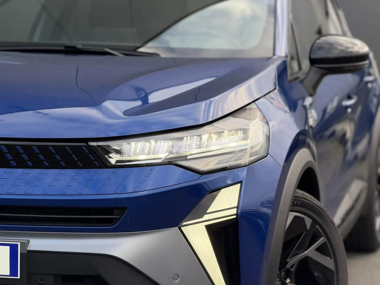 Gros plan sur l'avant droit du Renault Captur Bleu Iron, mettant en valeur le phare LED et la calandre moderne.