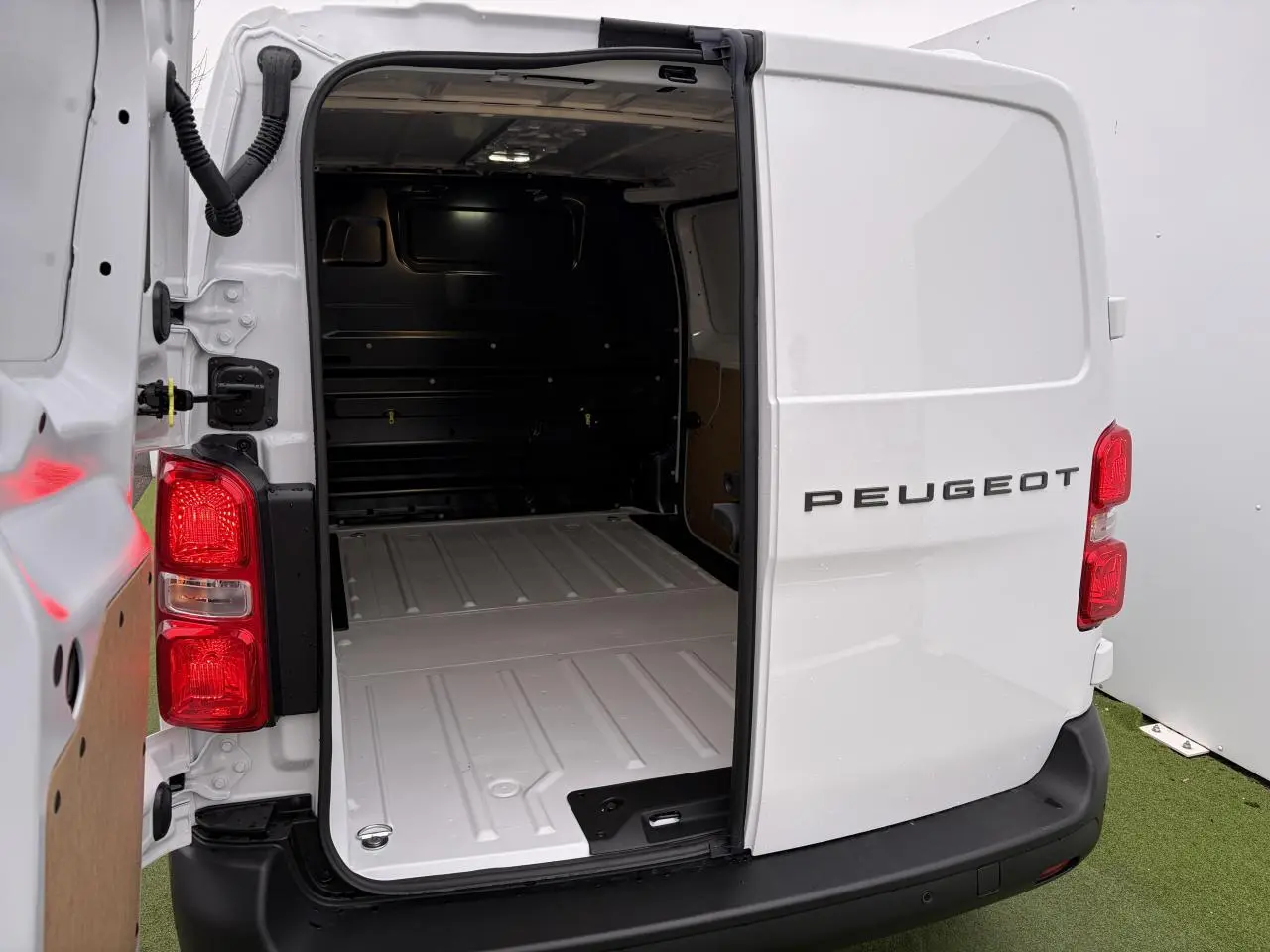 Vue arrière droite d’un Peugeot Expert Fourgon blanc Icy avec portes arrière ouvertes montrant l’espace de chargement éclairé.