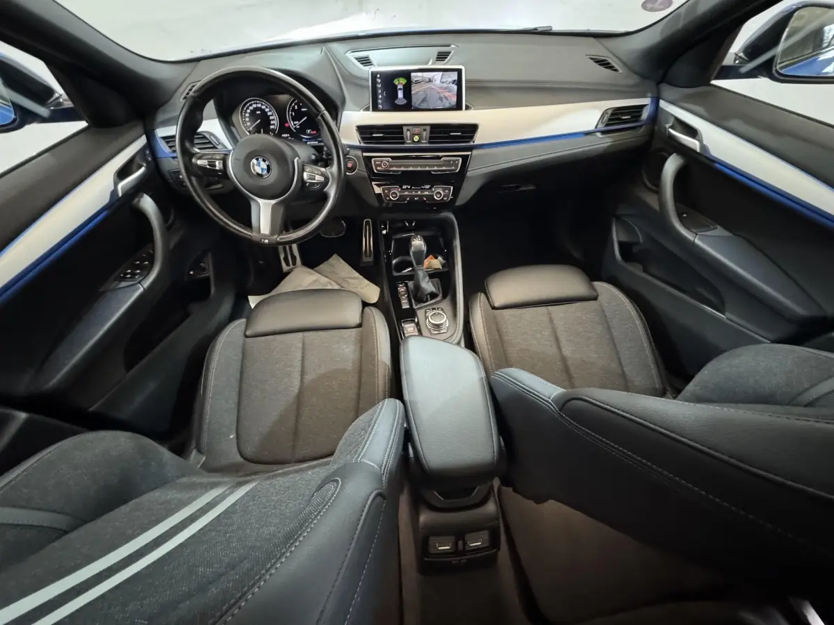 Vue intérieure avant de la BMW X2 bleu, montrant le tableau de bord, volant multifonctions et écran central avec caméra de recul.