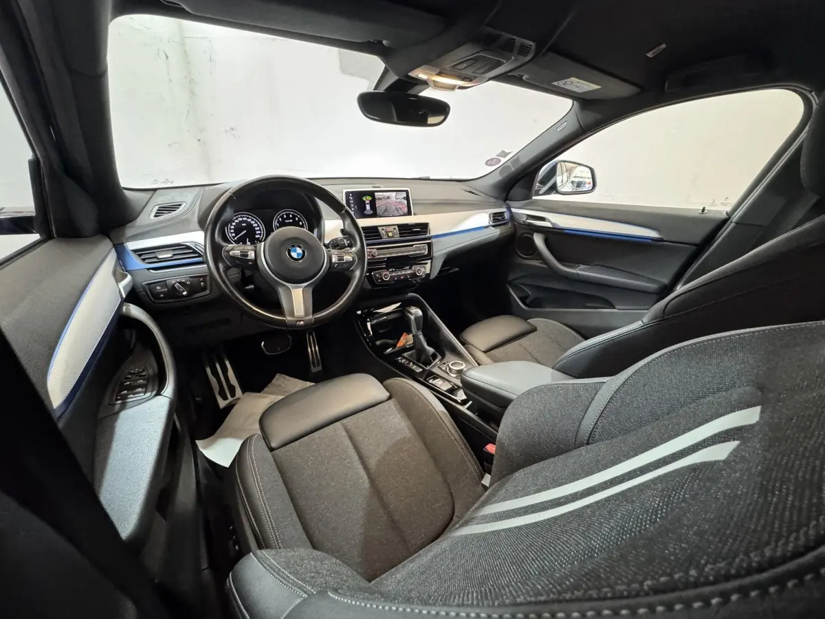 Intérieur BMW X2 xDrive25e M Sport 2021 vu côté conducteur, sièges noirs et bandeau bleu sur tableau de bord.
