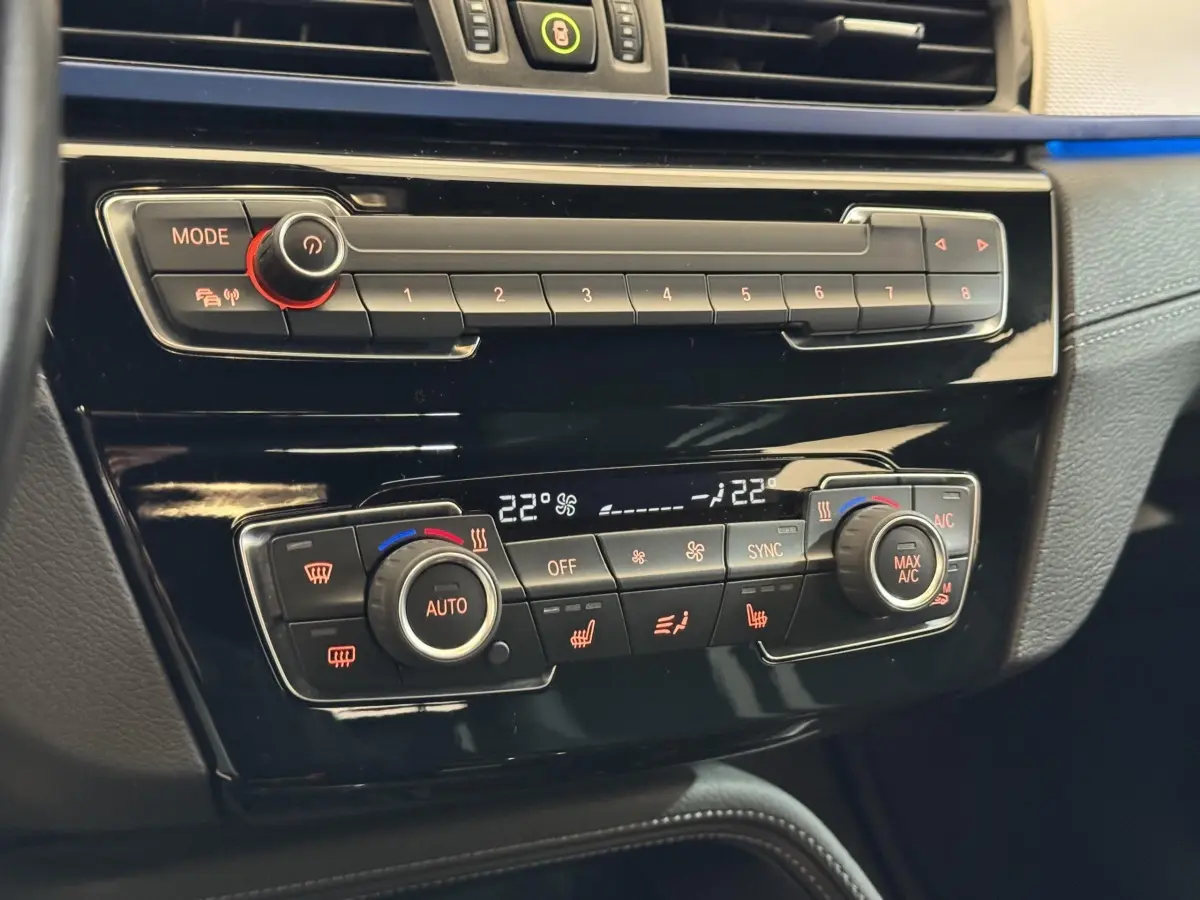 Gros plan sur la console centrale noire du BMW X2 xDrive25e 2021, montrant la climatisation automatique bi-zone et les commandes digitales.