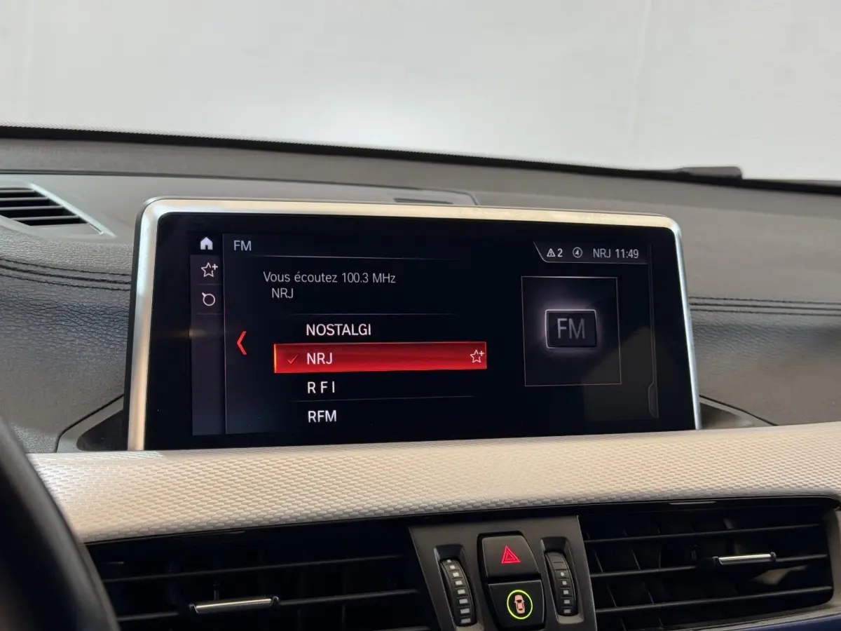 Écran central tactile du tableau de bord de la BMW X2 xDrive25e M Sport, affichant les stations radio FM.