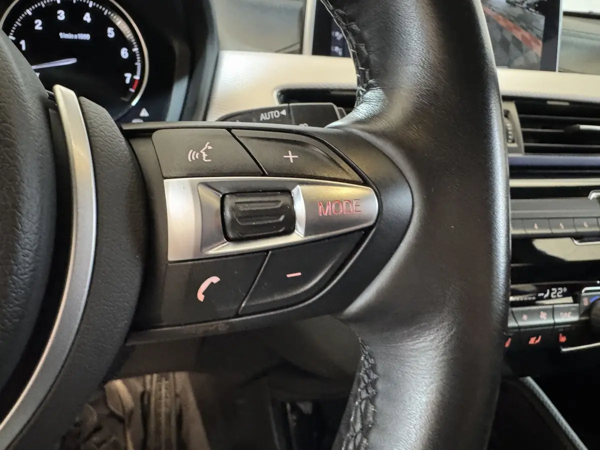 Gros plan sur les commandes multifonctions du volant cuir noir du BMW X2 xDrive25e M Sport 2021, intérieur moderne.