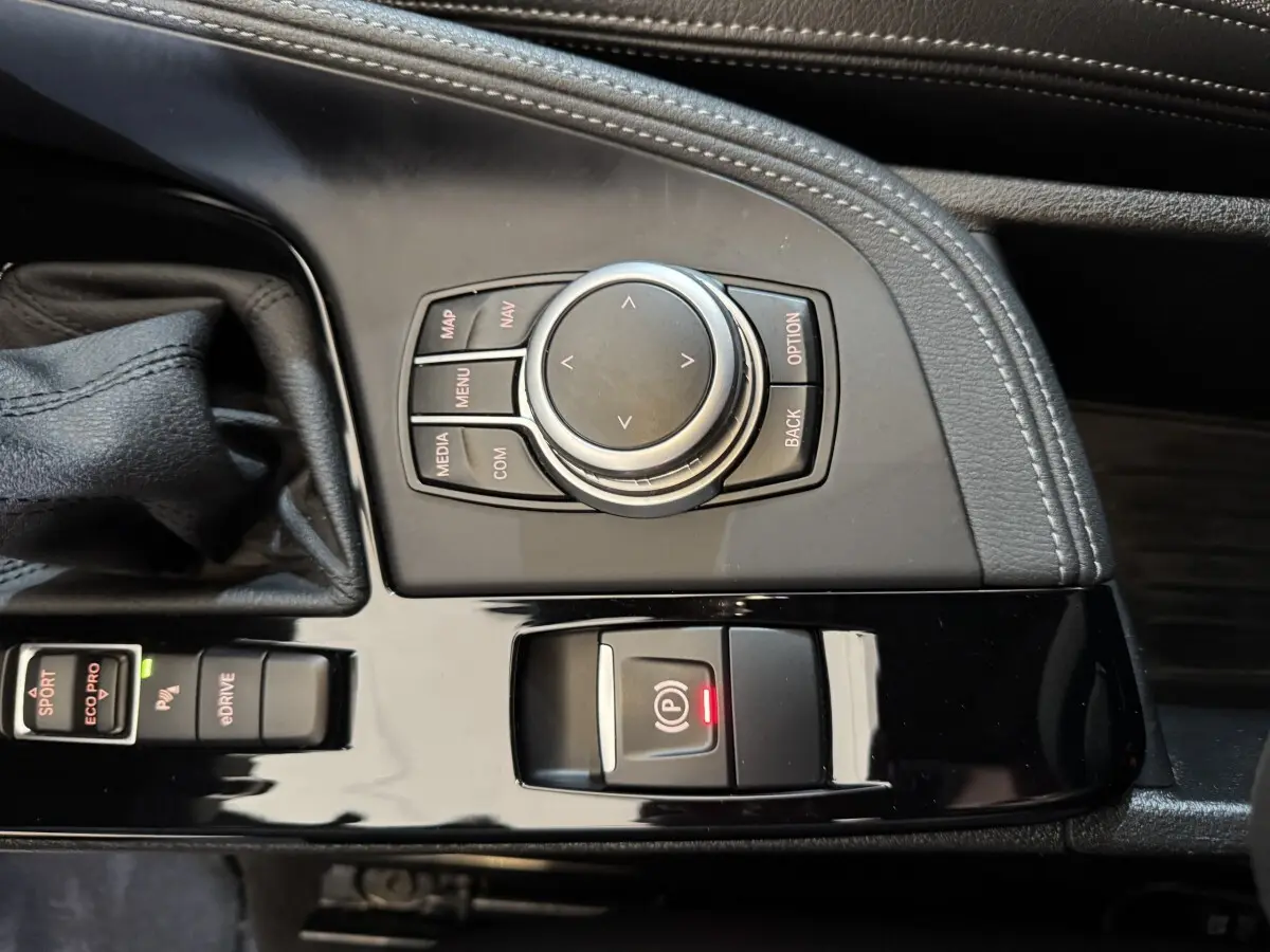 Vue rapprochée de la console centrale noire avec commandes multimédia et frein à main électrique du BMW X2 bleu.