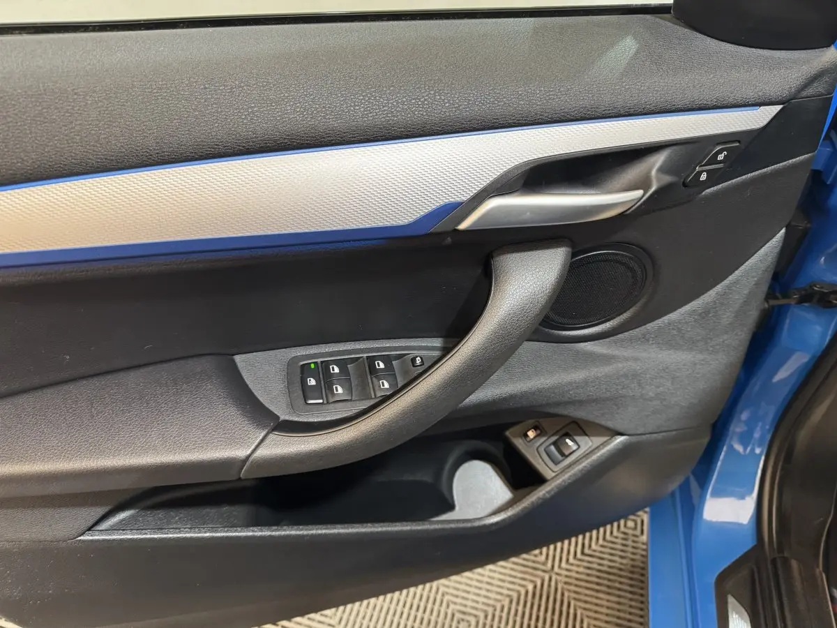 Vue rapprochée de la porte avant gauche bleu électrique du BMW X2 xDrive25e M Sport avec commandes de vitres et poignée noire.