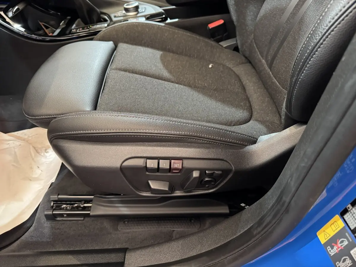 Gros plan sur le siège avant gauche noir avec réglages électriques, bordure de portière bleu visible d’une BMW X2 hybride.