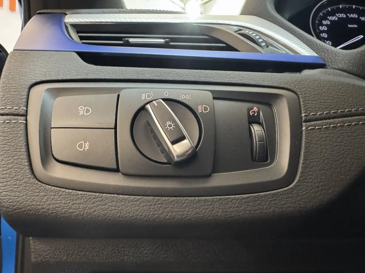 Détail du panneau de commandes d’éclairage sur tableau de bord noir avec insert bleu d’une BMW X2 xDrive25e M Sport 2021.