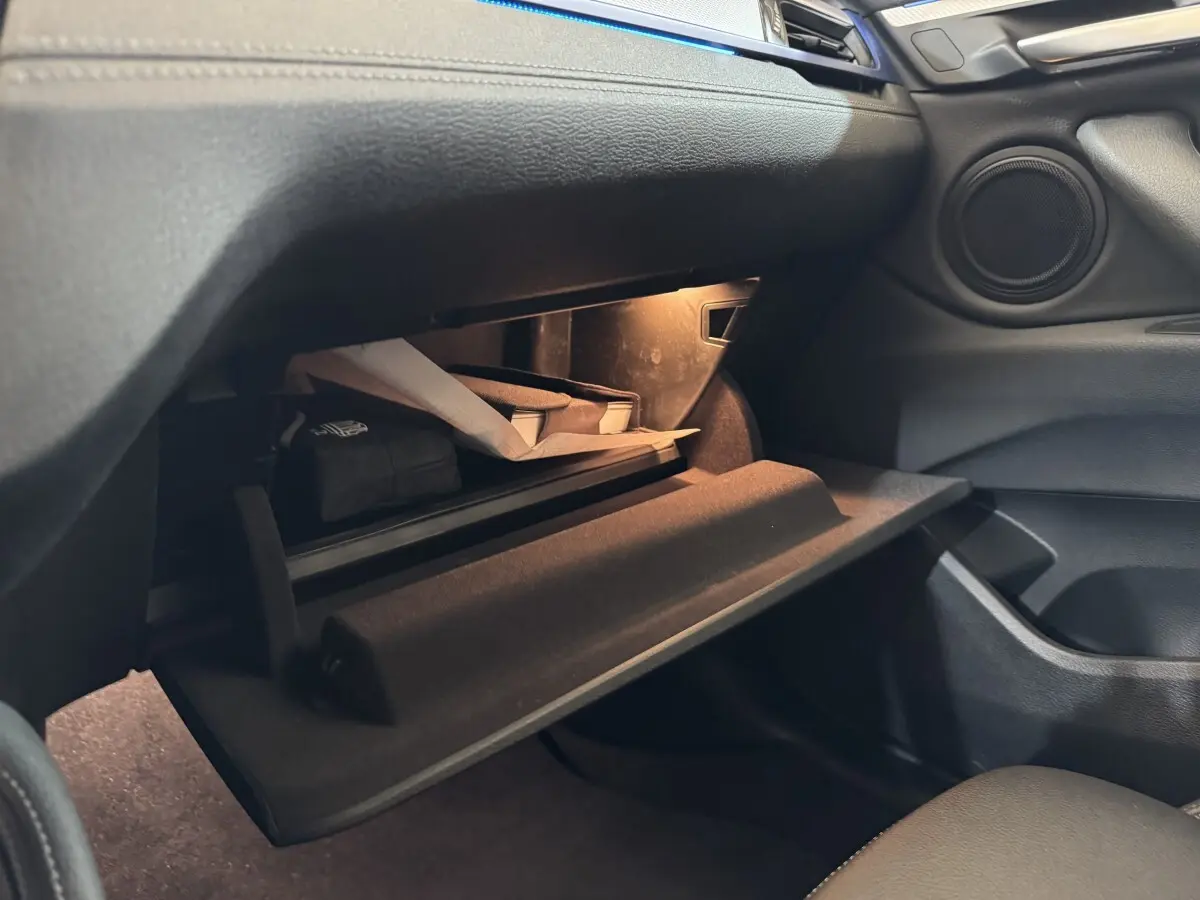 Vue intérieure sur la boîte à gants ouverte du BMW X2 xDrive25e M Sport 2021, avec éclairage intérieur et rangements visibles.