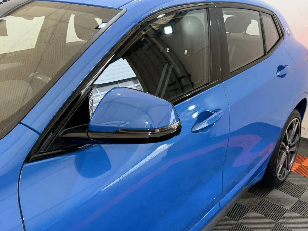 Vue côté gauche rapprochée du BMW X2 xDrive25e M Sport bleu, mettant en valeur la portière et le rétroviseur.