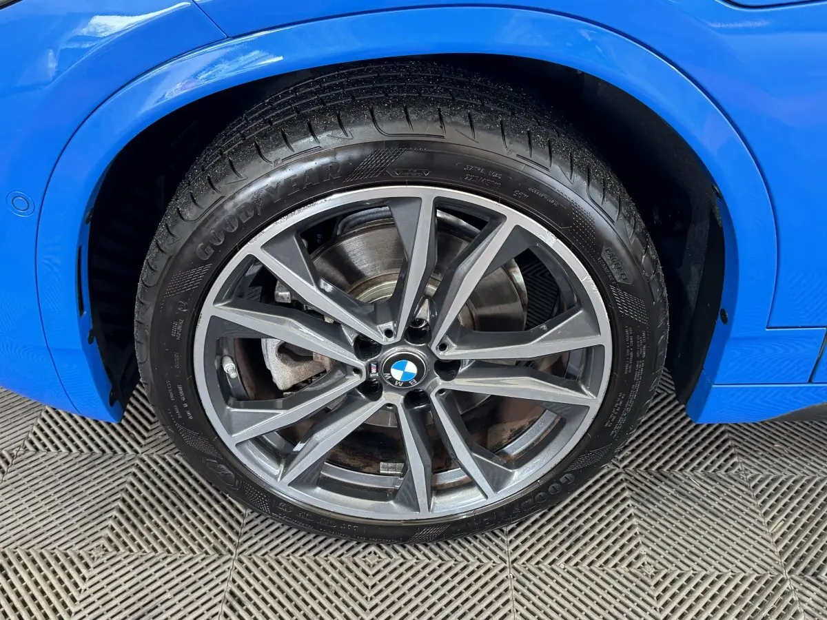 Gros plan sur la roue avant droite d'une BMW X2 bleu électrique avec jante alliage et pneu Goodyear.