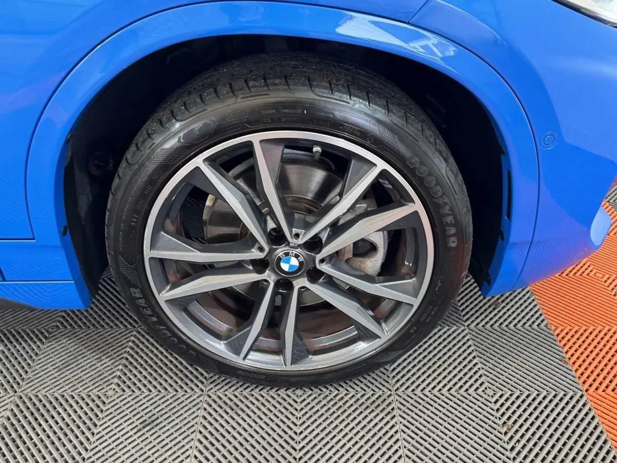 Gros plan sur la roue avant droite d’une BMW X2 bleu électrique, mettant en valeur la jante alliage moderne.