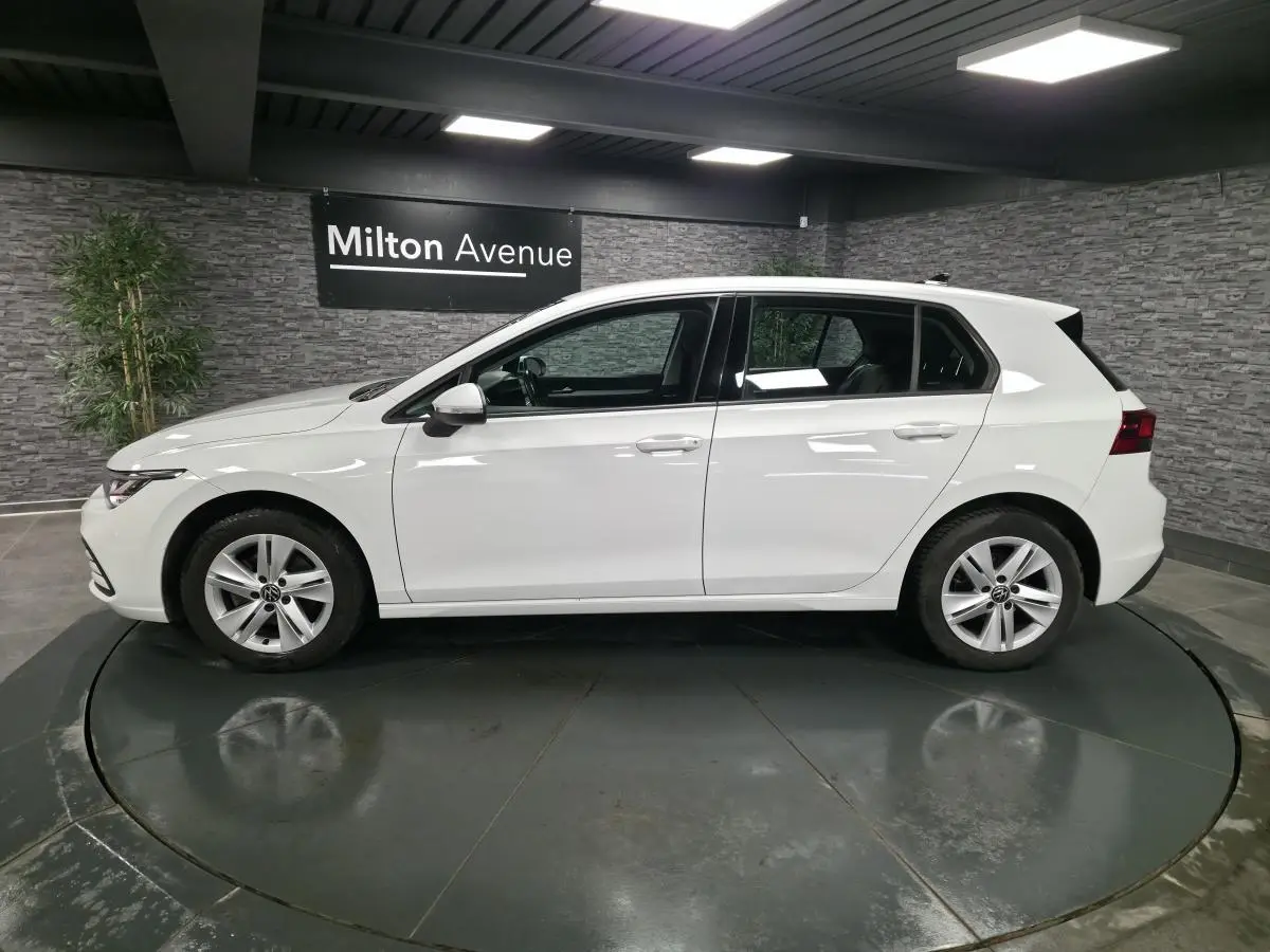 Vue de profil côté gauche d'une Volkswagen Golf VIII blanche, avec jantes alliage et poignées couleur carrosserie.